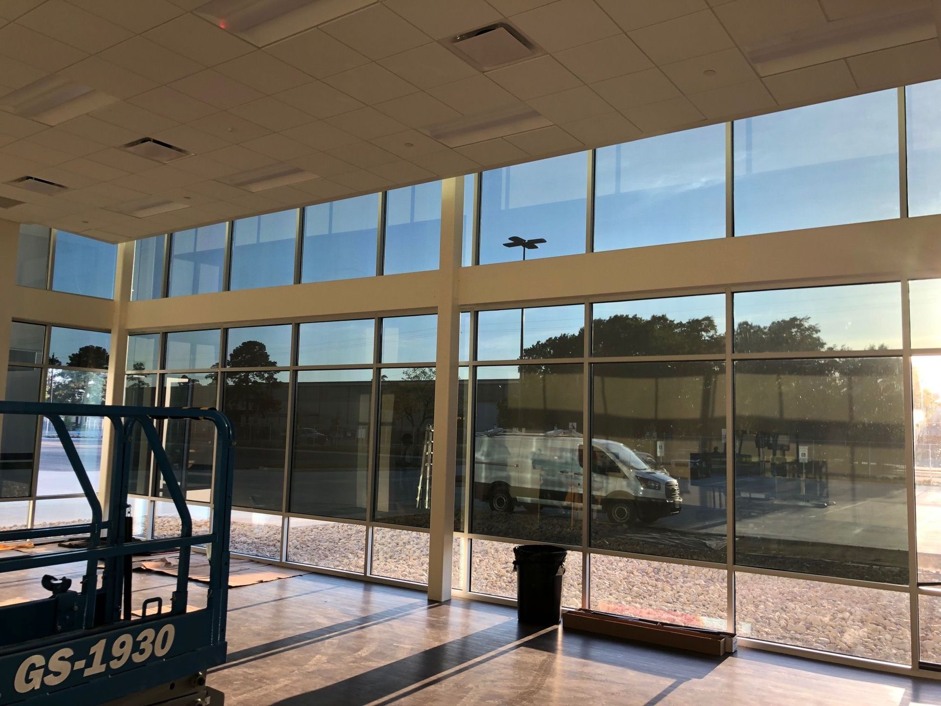 Interior view of a building with large windows, a lift, and outdoor scenery reflecting.