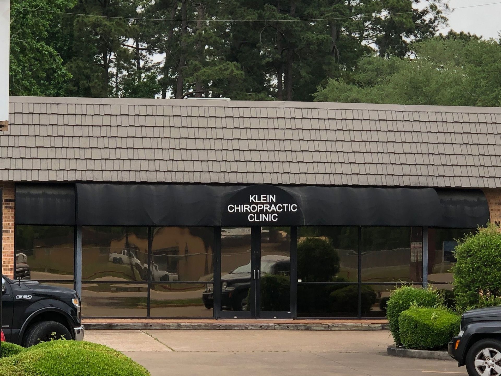 A chiropractic clinic with a brown roof and tinted windows, black awning. Parked cars are in front of the building.