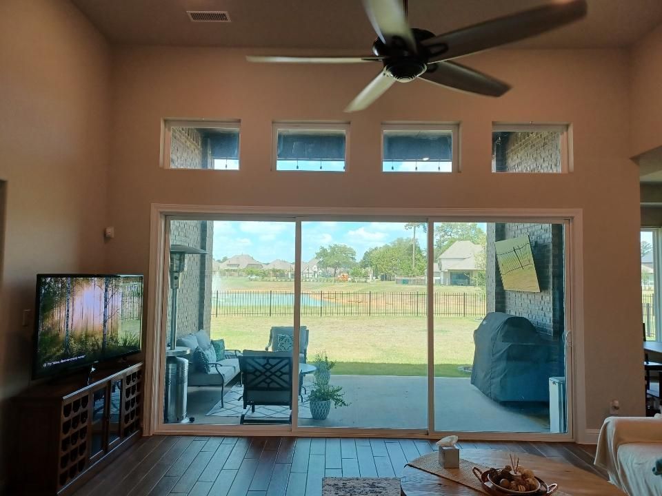 Living room with large sliding glass doors overlooking a patio and lake. TV on a cabinet, ceiling fan.