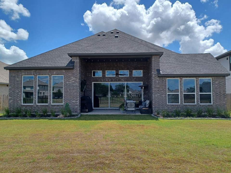 Back of a brick house with multiple windows, a sliding glass door, and a grassy backyard under a cloudy sky.