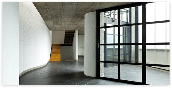 Modern interior with curved white wall, black flooring, glass door, and wooden stairs.