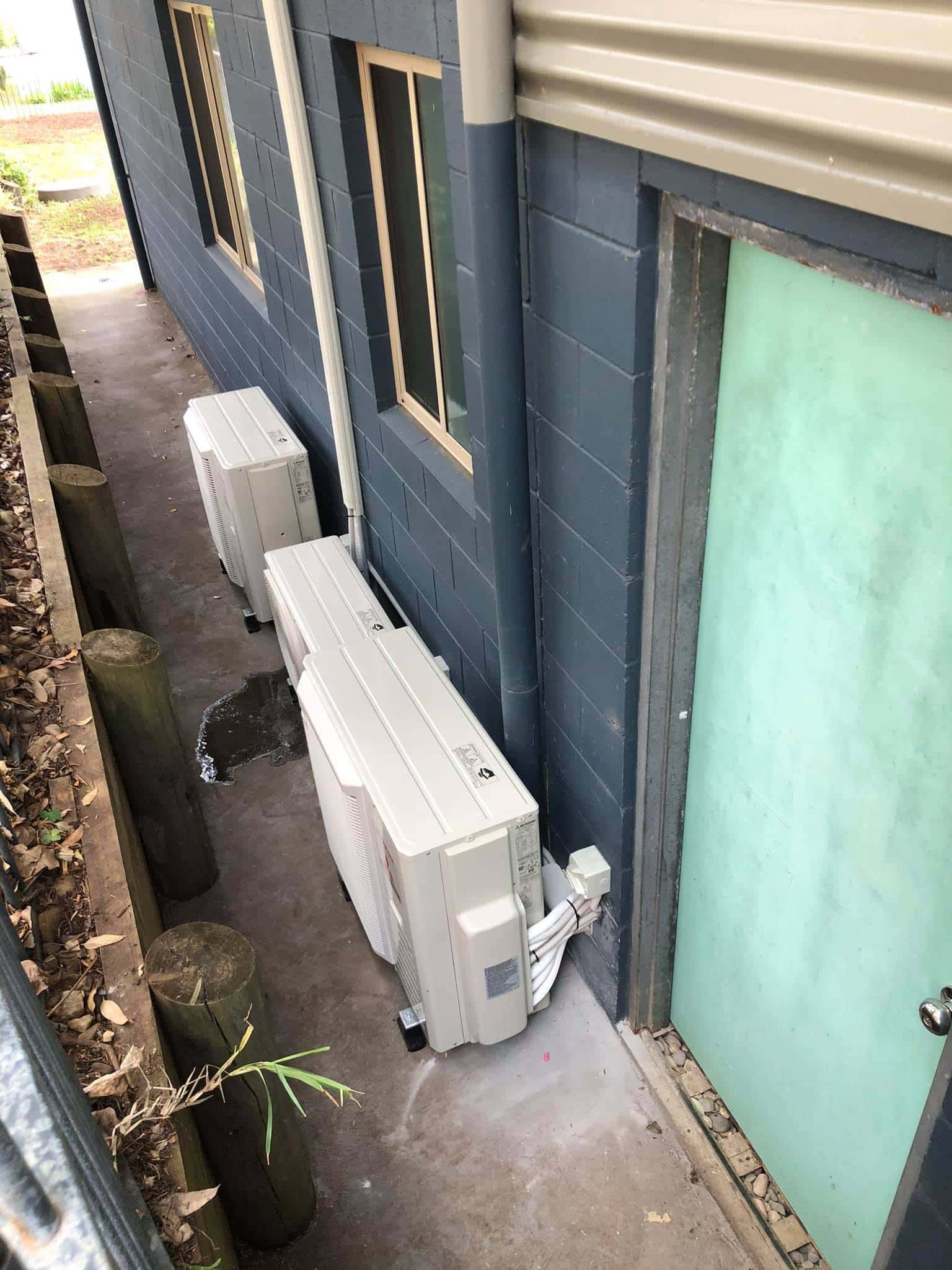Two Air Conditioners Are Sitting on the Side of a Building Next to a Door — Steve's Air Conditioning in Lakeside Dr, NSW