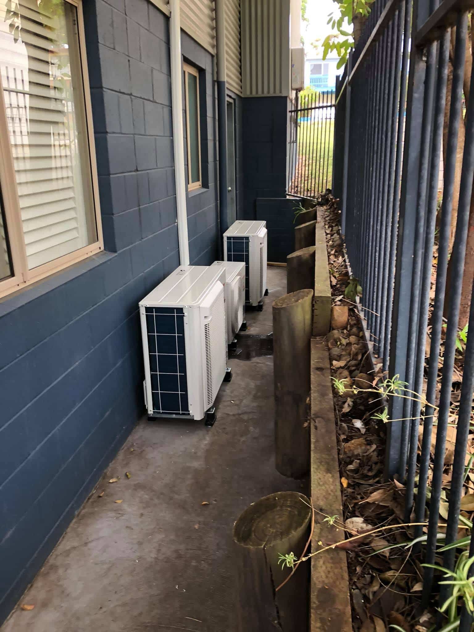 A Row of Air Conditioners Are Sitting on the Side of a Building Next to a Fence — Steve's Air Conditioning in Lakeside Dr, NSW