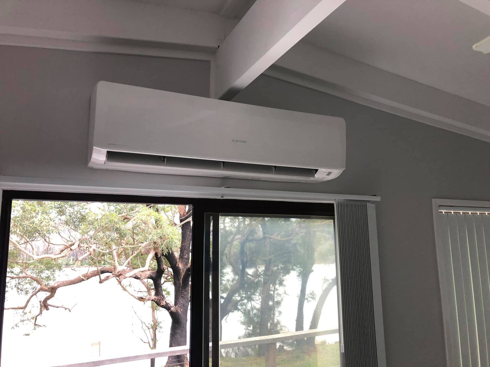 A White Air Conditioner is Hanging From the Ceiling Above a Window — Steve's Air Conditioning in Lakeside Dr, NSW