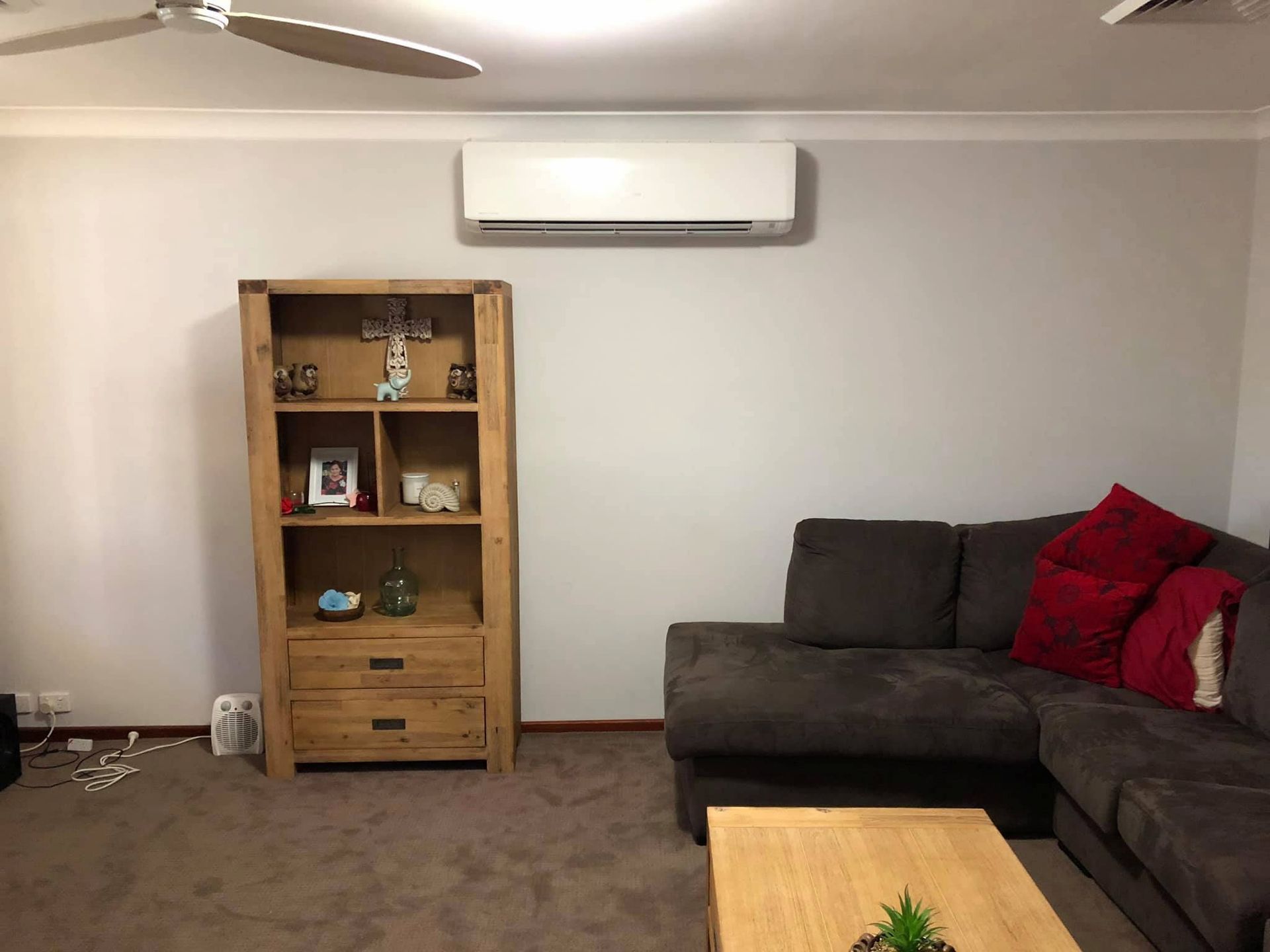 A Living Room With a Couch, Coffee Table, Bookshelf and Ceiling Fan — Steve's Air Conditioning in Thirroul, NSW