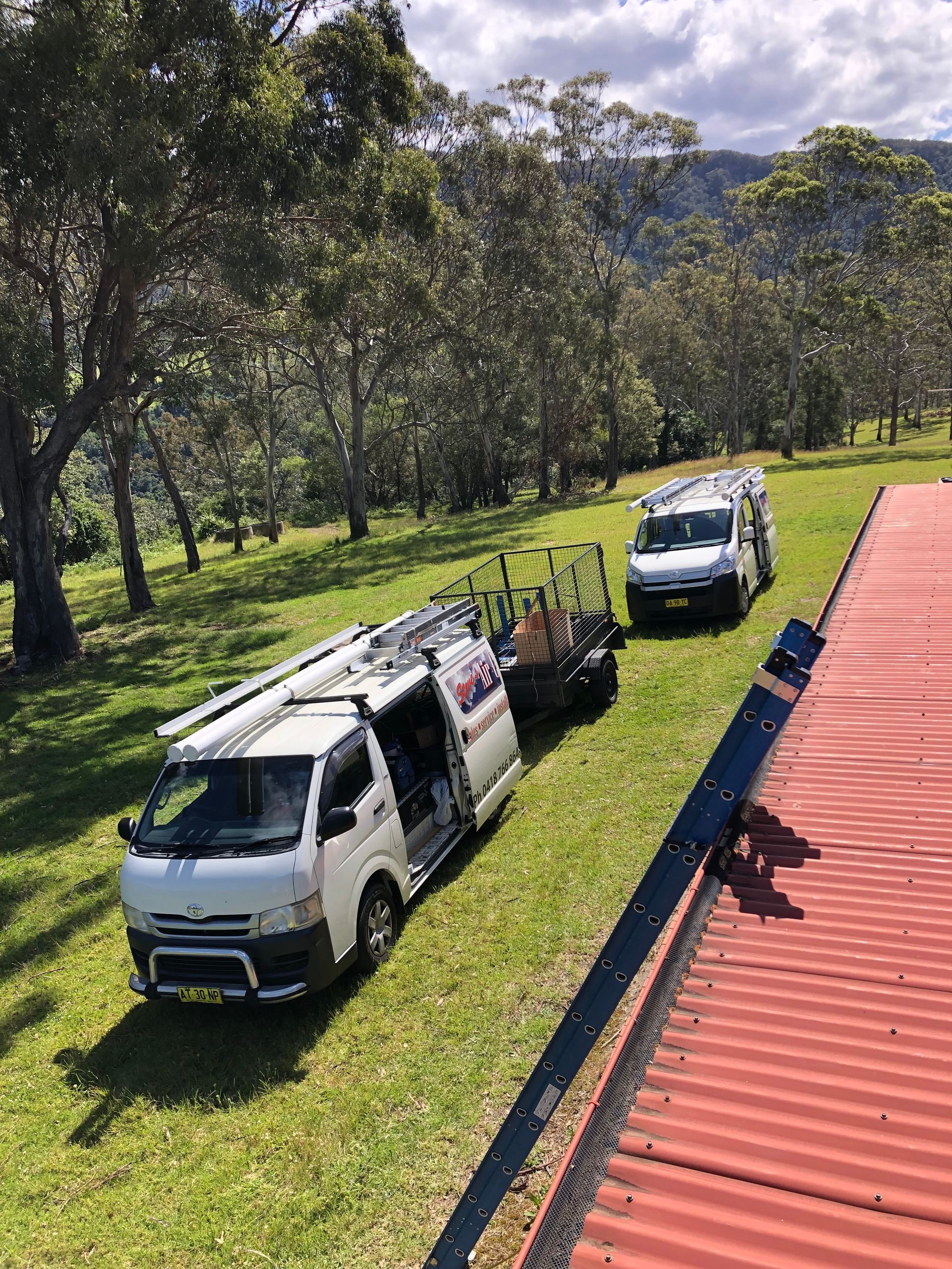 Three vans are parked in a grassy field next to a red roof.
