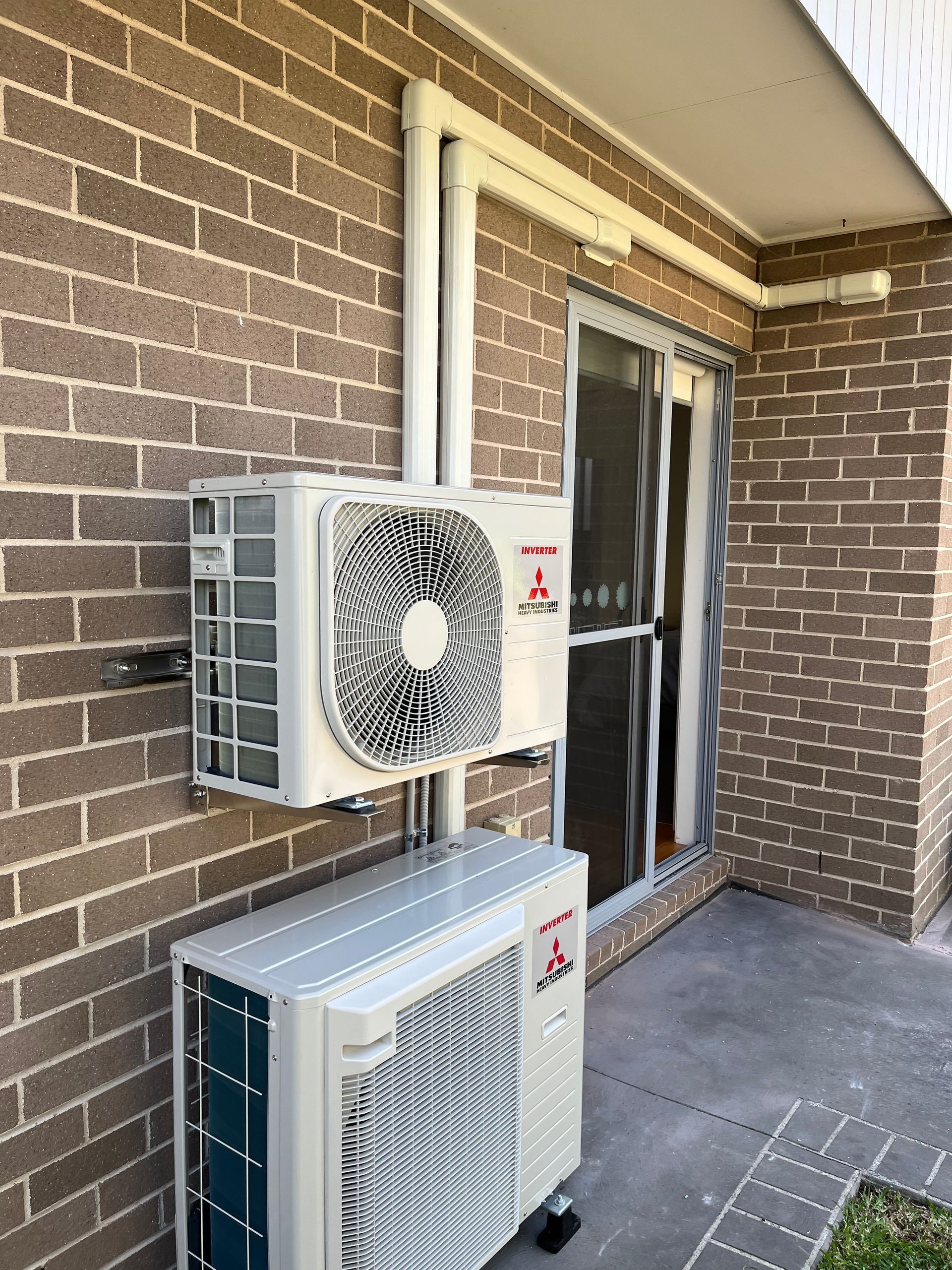 Two air conditioners are mounted on the side of a brick building.
