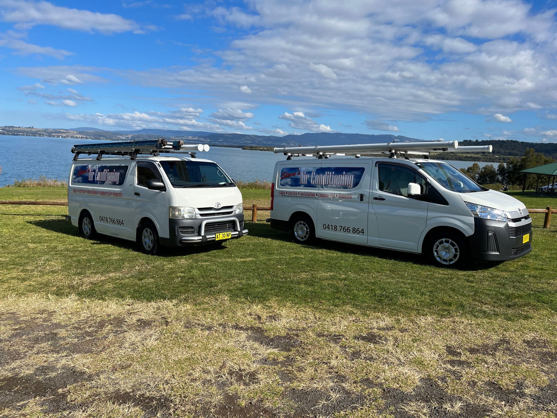 Two white vans are parked in a grassy field next to a body of water.