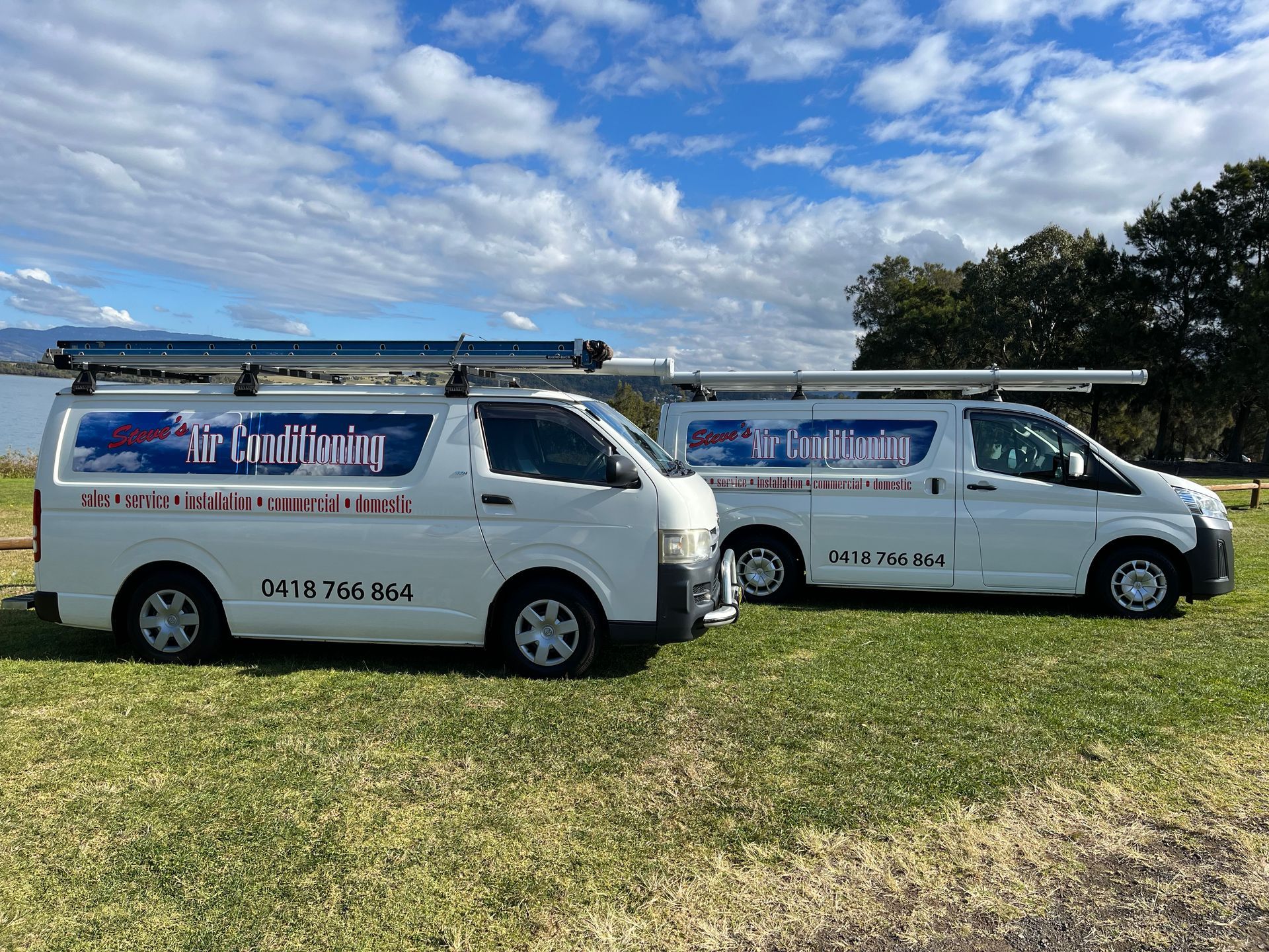 Two white vans are parked next to each other in a grassy field.