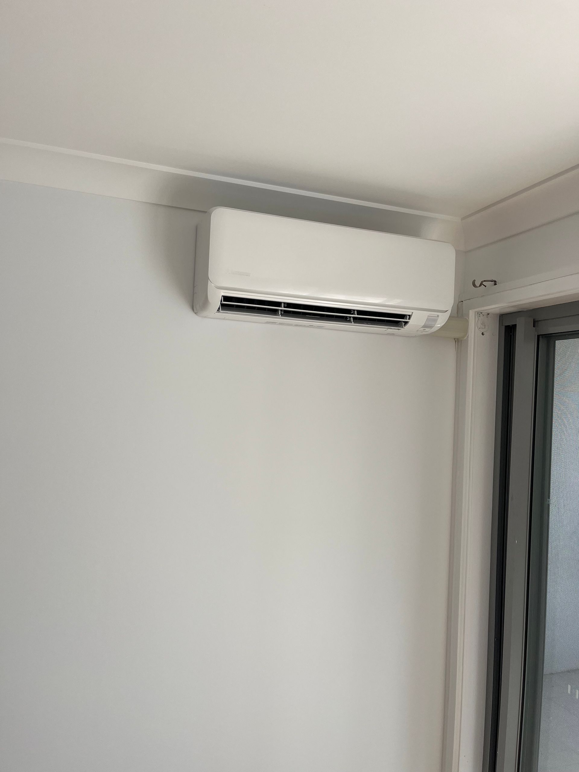 A white air conditioner is mounted on a white wall next to a window.