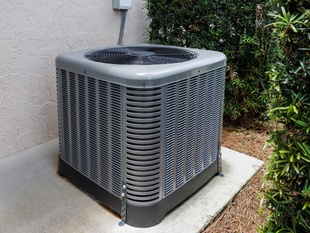 Central air conditioning unit outside a building, surrounded by greenery.