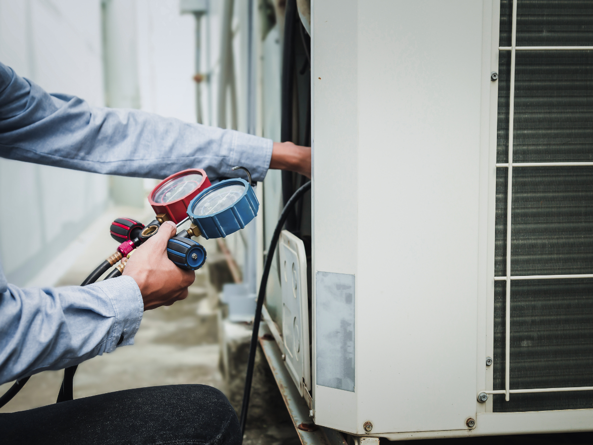 HVAC technician using gauges to service an air conditioning unit outdoors.
