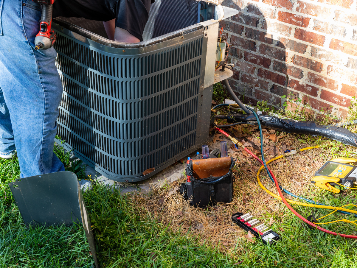 HVAC technician working on an outdoor air conditioning unit next to a brick building.