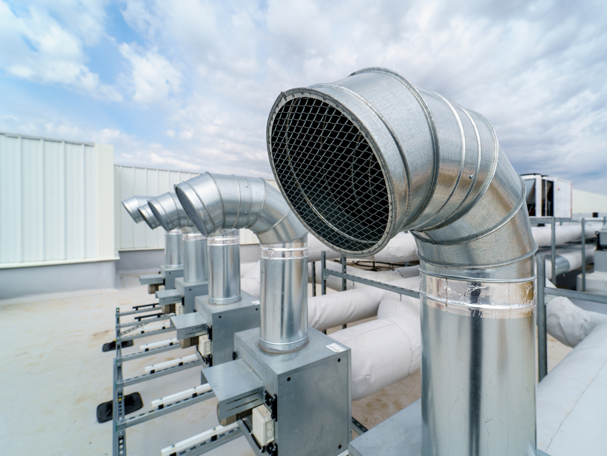 Rooftop HVAC system with silver metal vents angled toward the sky, against a white building and cloudy blue sky.