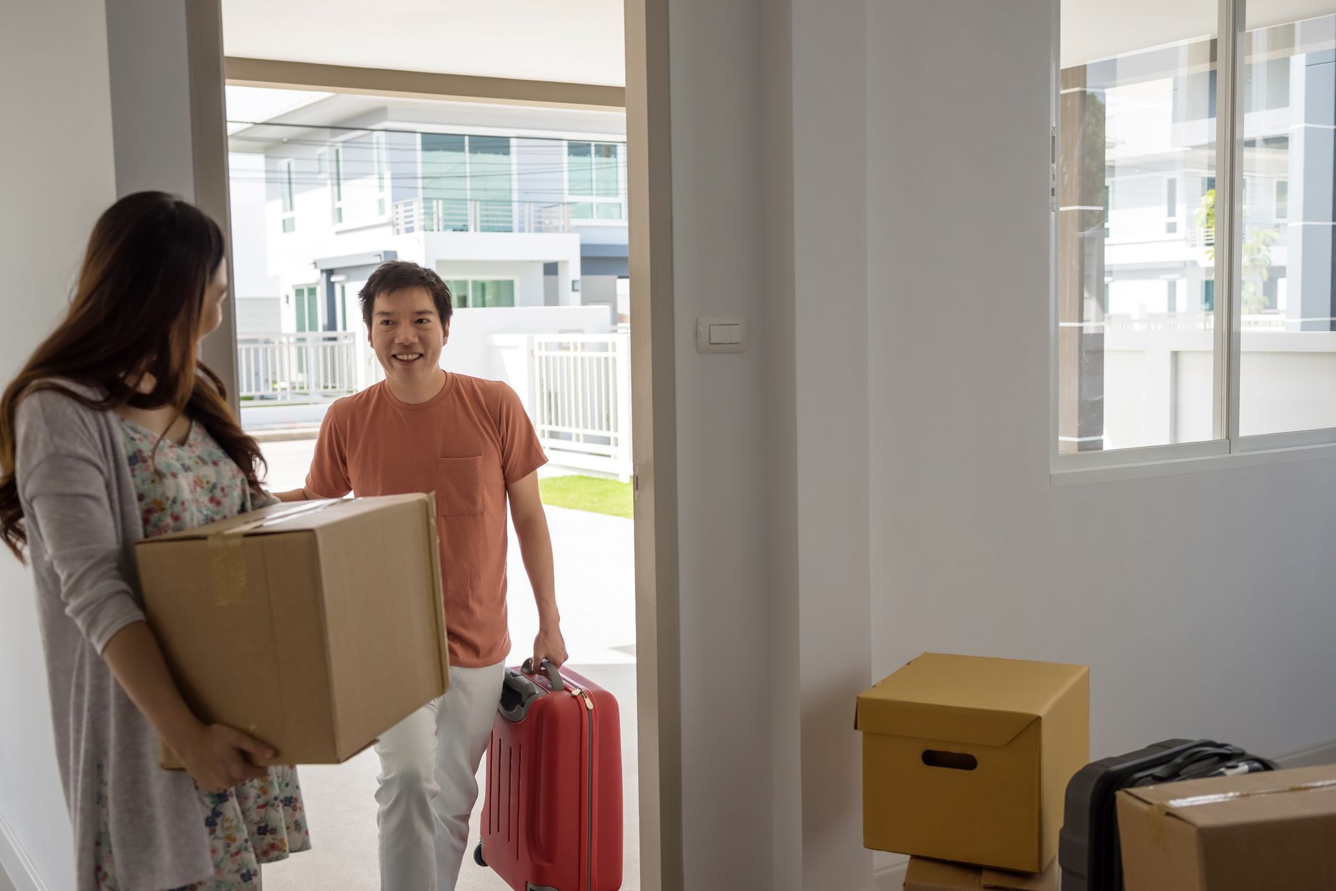 A man and a woman are carrying boxes and luggage into a new home.