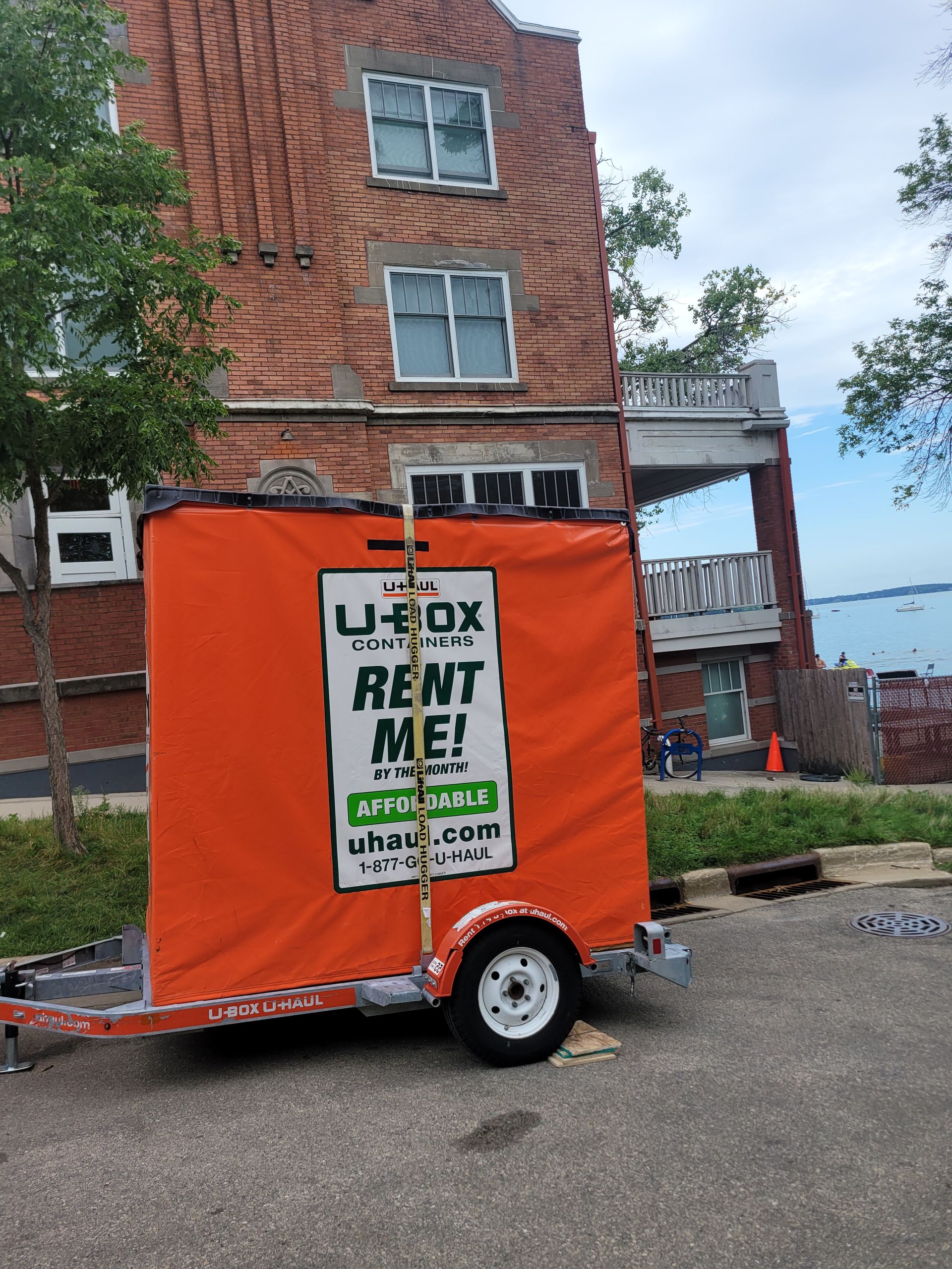 An orange u-box trailer is parked in front of a brick building