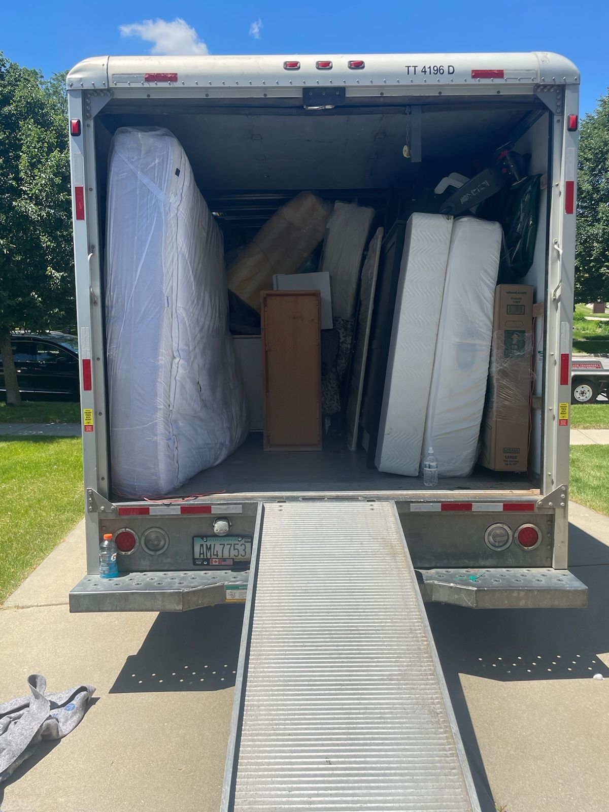 Moving truck interior packed with wrapped mattresses, furniture, and boxes; ramp extended.
