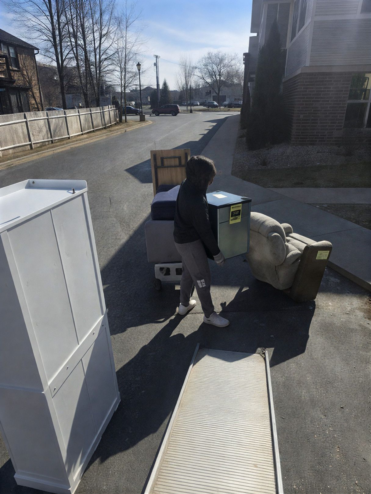 Person carrying a box, moving furniture outdoors on a sunny day.