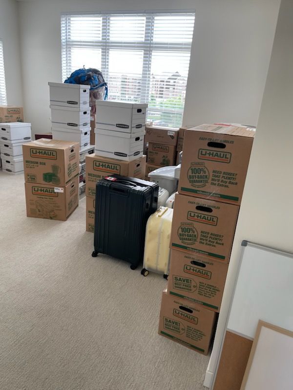 Boxes and luggage stacked in a room with a window, indicating a move or storage.