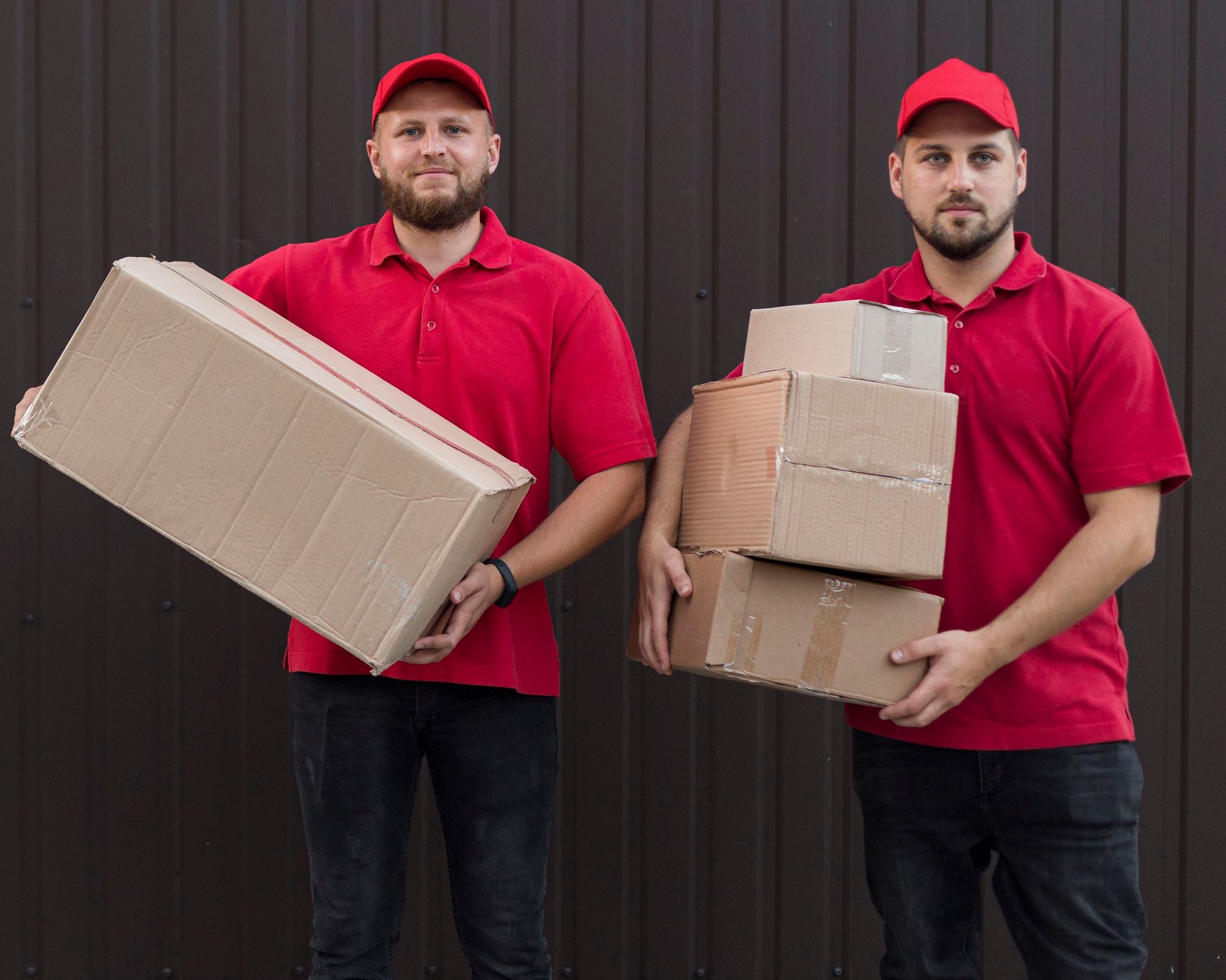 Two delivery men in red shirts are holding boxes in their hands.