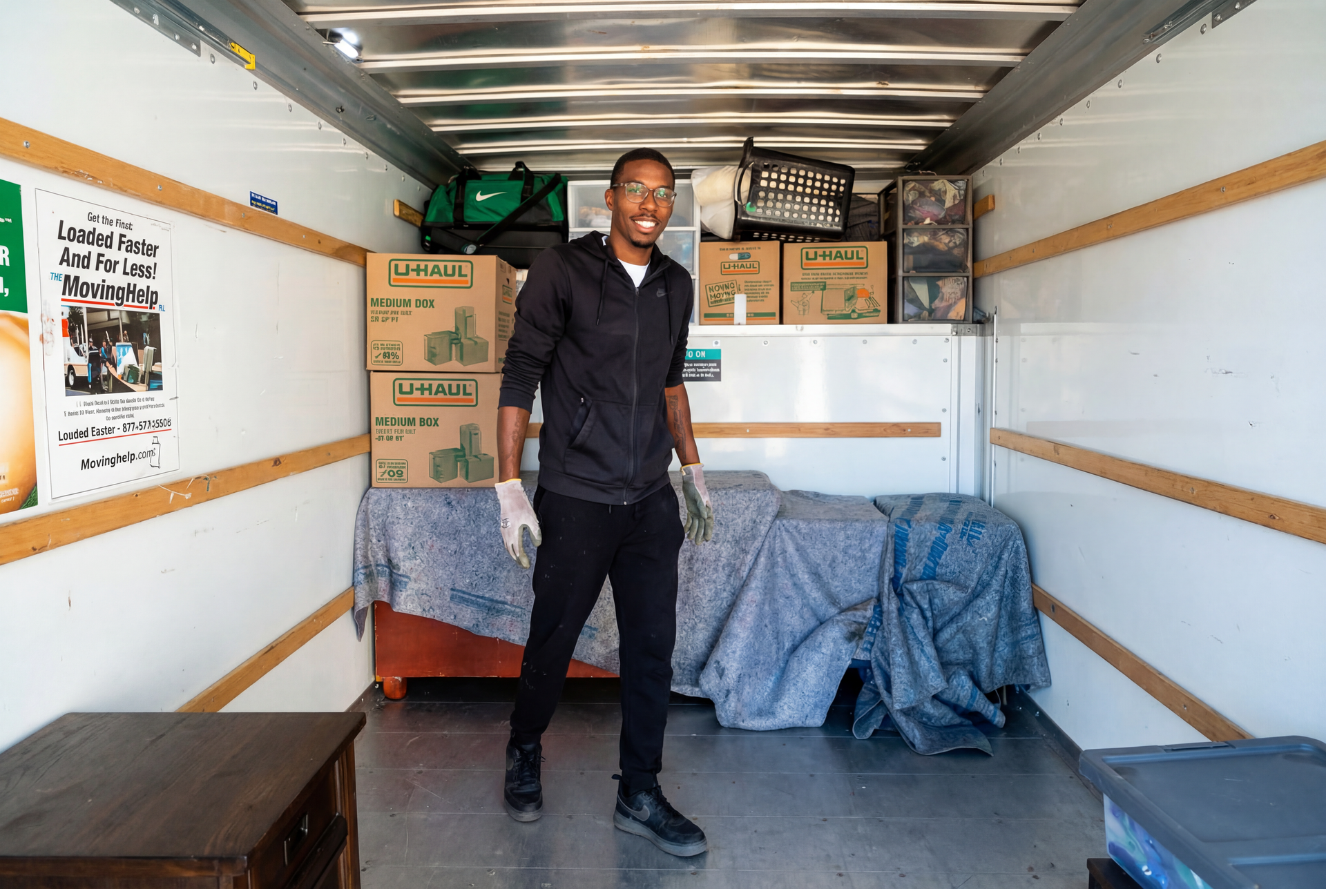 Man standing in a moving truck, holding items. Boxes and furniture inside the truck.