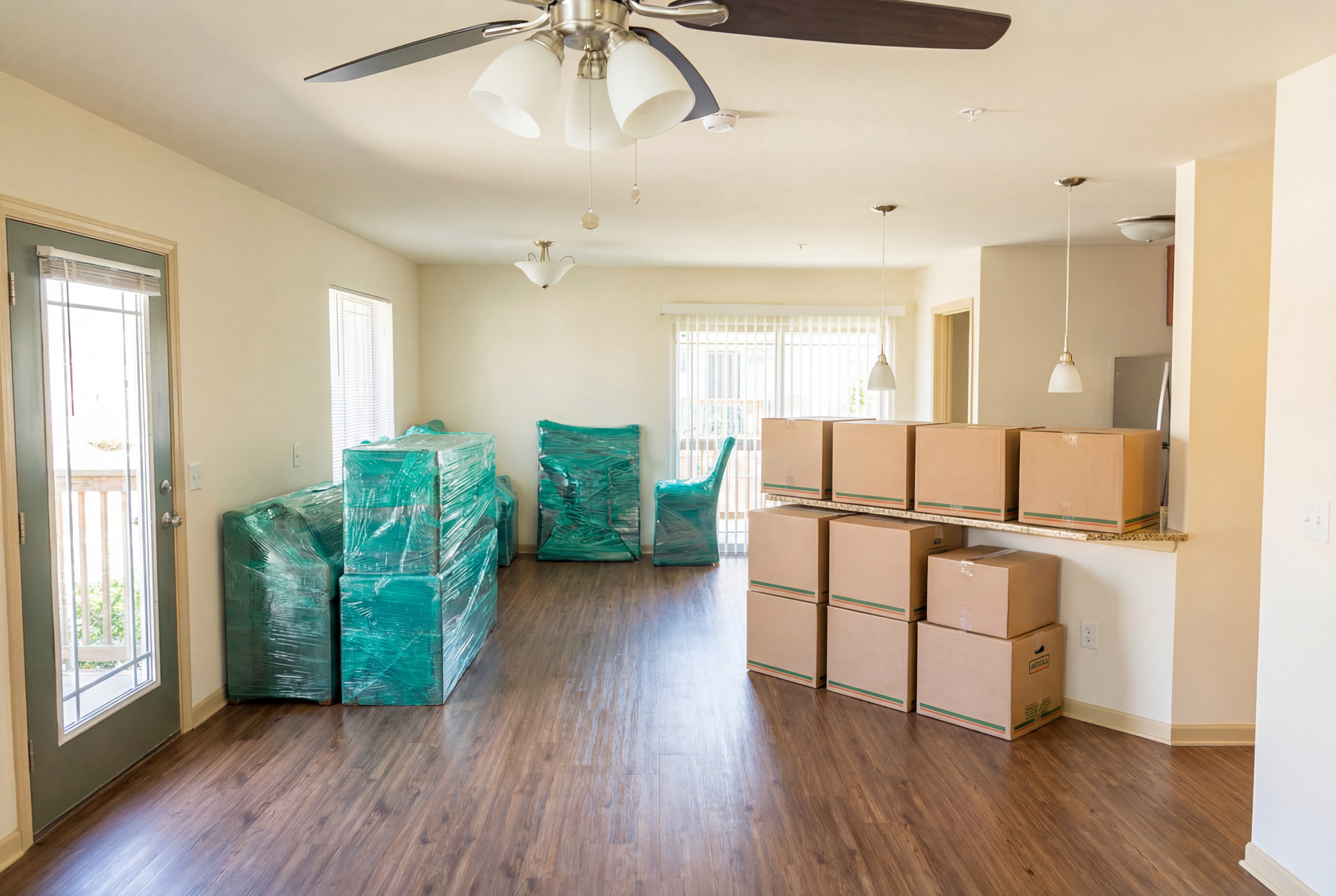 Empty apartment interior, cardboard boxes, furniture wrapped in plastic, wooden floor, open door.