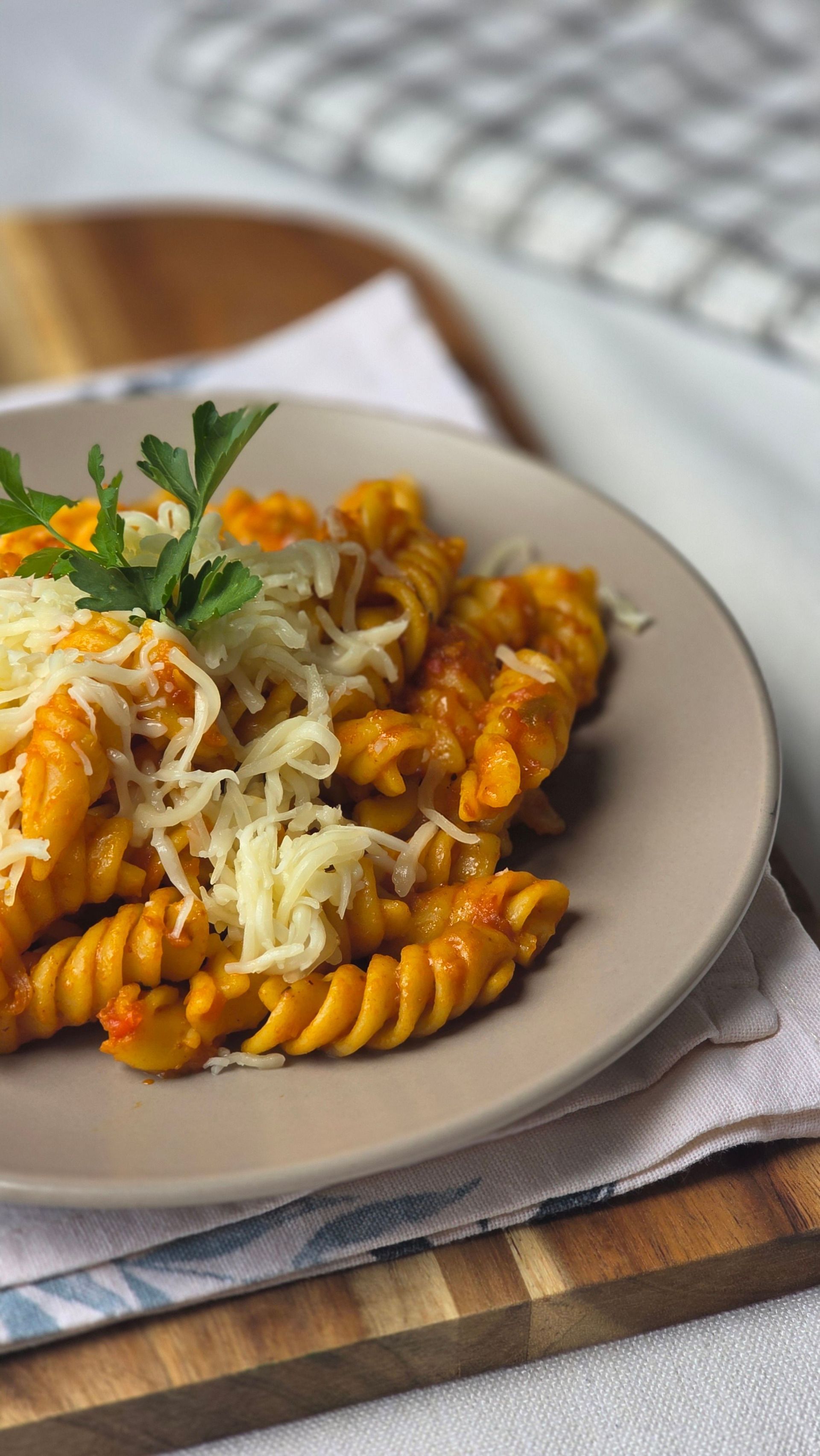 Pasta al sugo di pomodoro e formaggio grattugiato su un piatto, guarnita con prezzemolo su un tagliere di legno.