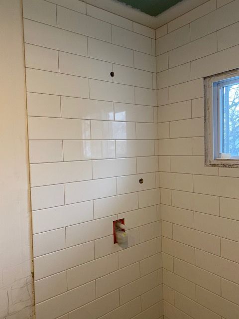 White subway tile shower walls with plumbing fixtures and a small window.