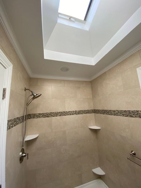 Bathroom with beige tiles, a skylight, shower fixtures, and built-in shelves.