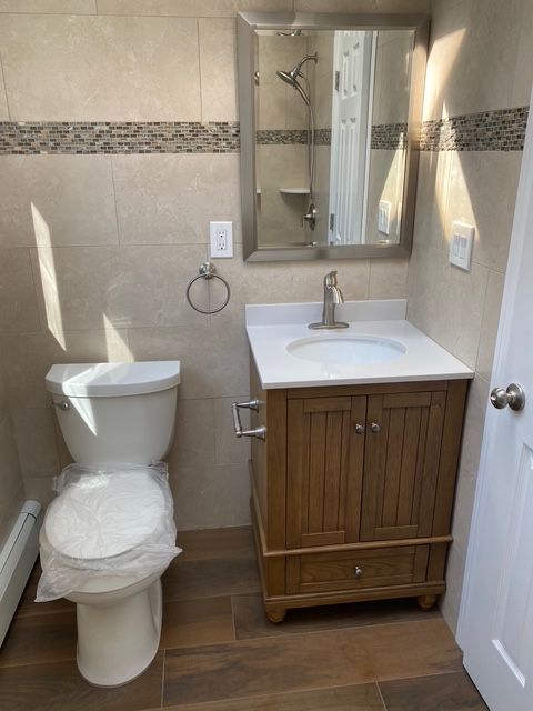 Bathroom with a toilet, vanity, and tiled walls. Brown wood tones and neutral colors.