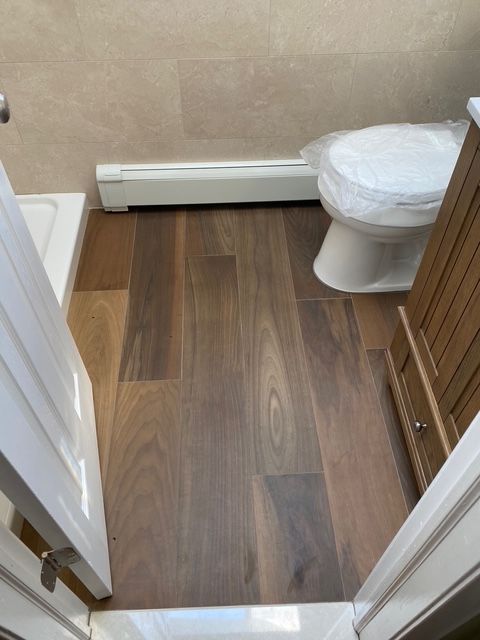 Bathroom with wood-look tile floor, toilet, and vanity. Beige wall tile, a radiator, and a white door frame.