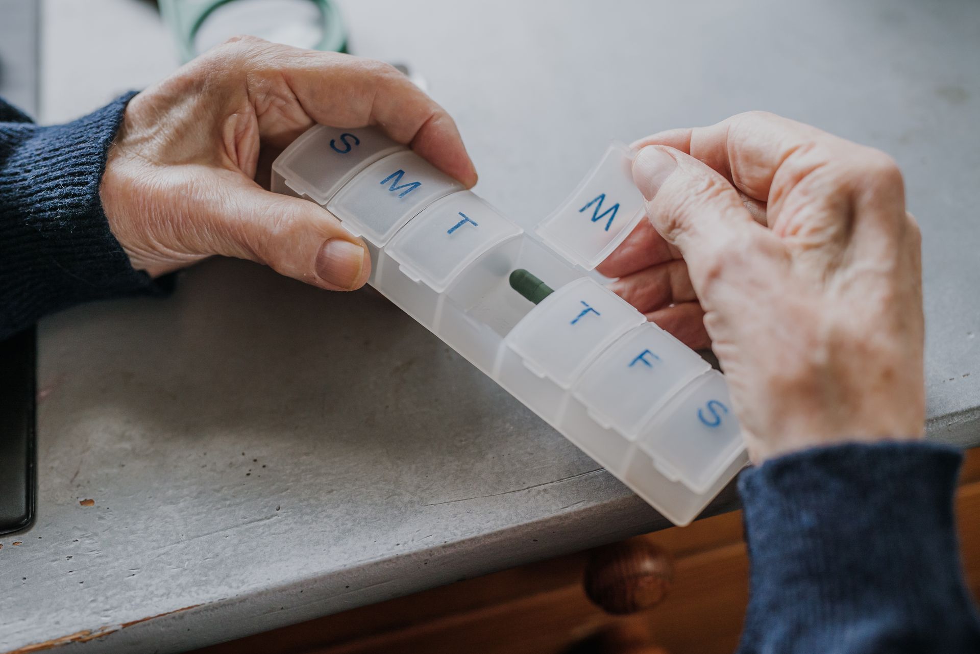 A person is taking a pill out of a pill holder.