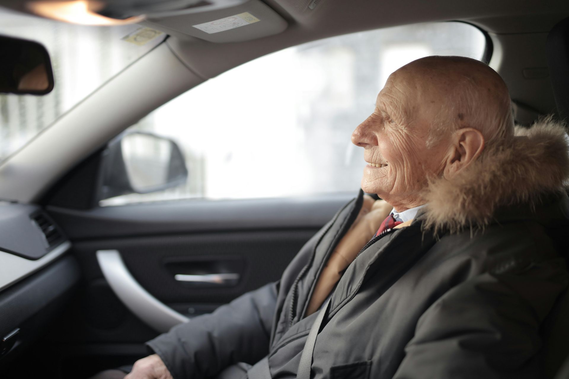 An elderly man is sitting in the driver 's seat of a car.