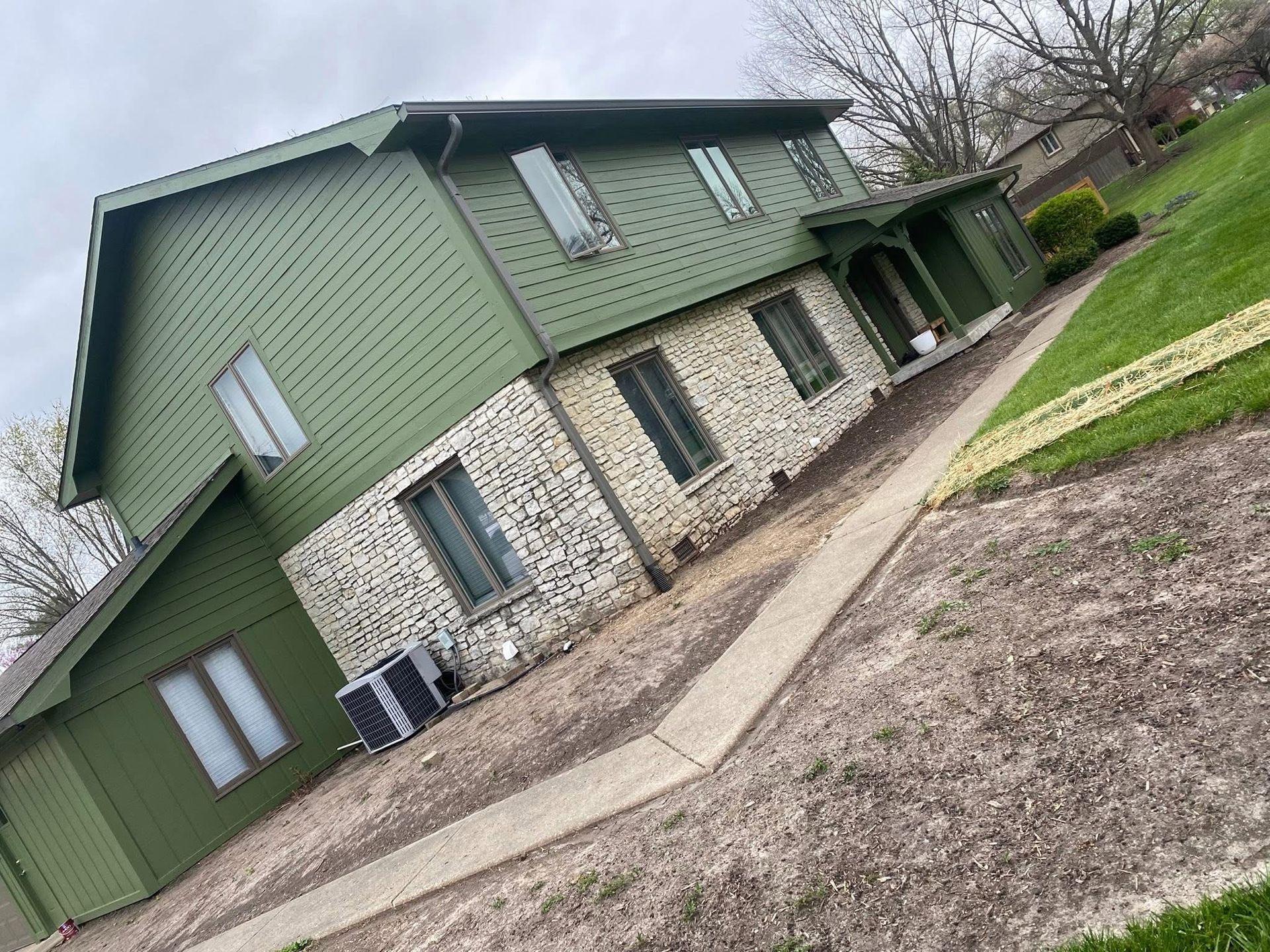 Two-story house with green siding and a brick facade, sidewalk leads to the front door.