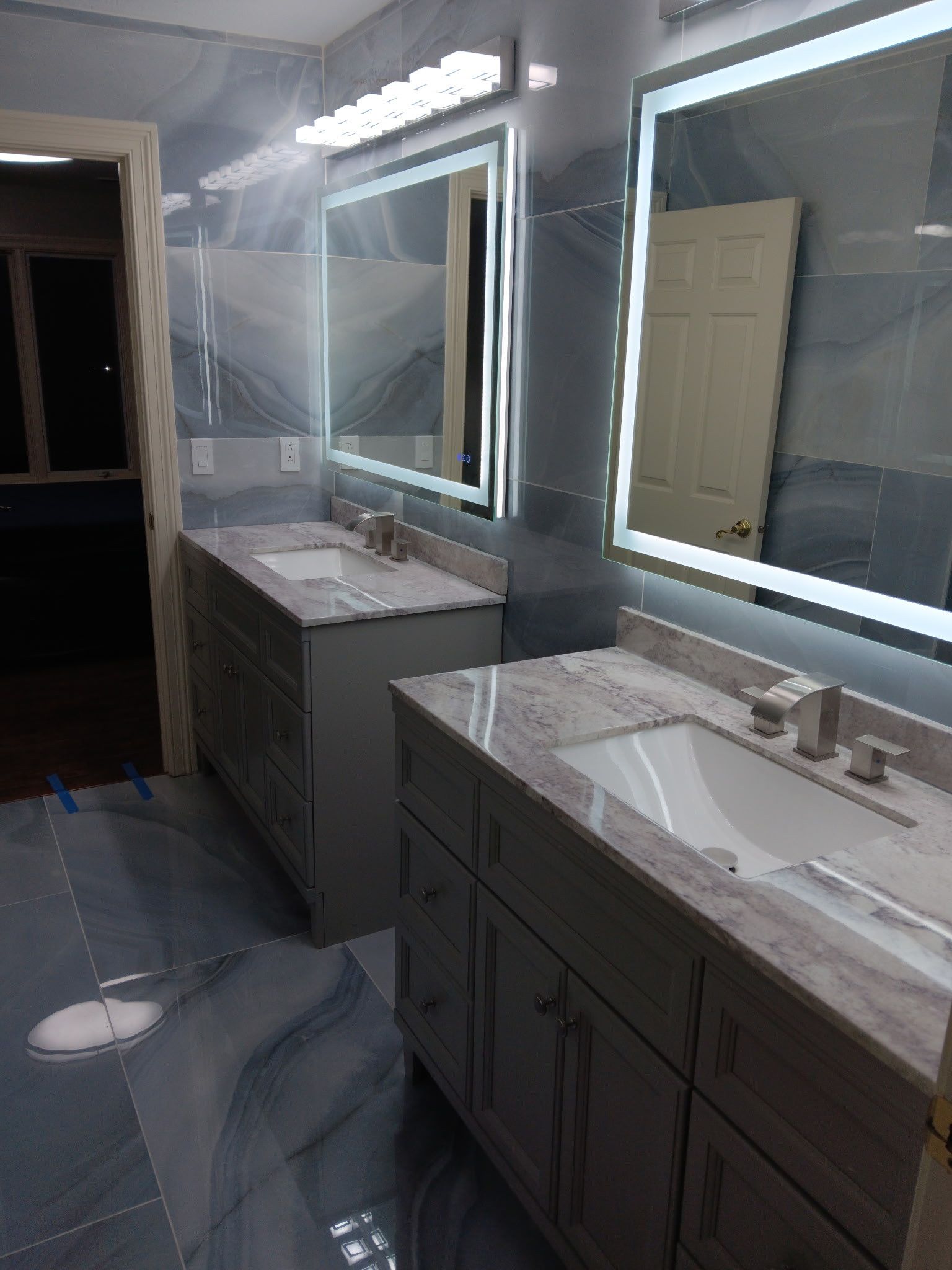 Modern bathroom with two vanities, illuminated mirrors, and blue-gray patterned tile.