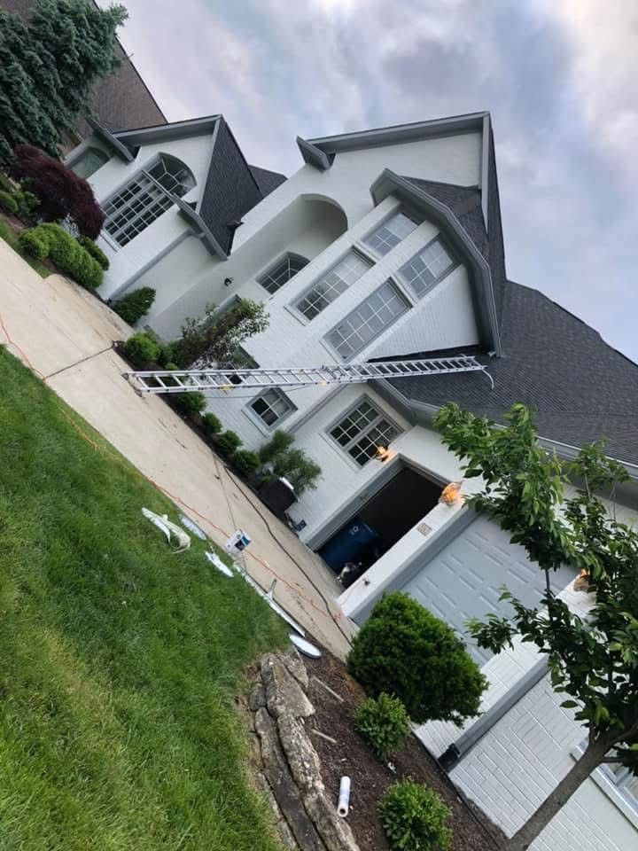 White house with ladder on the roof, garage door open, cloudy sky, green lawn.