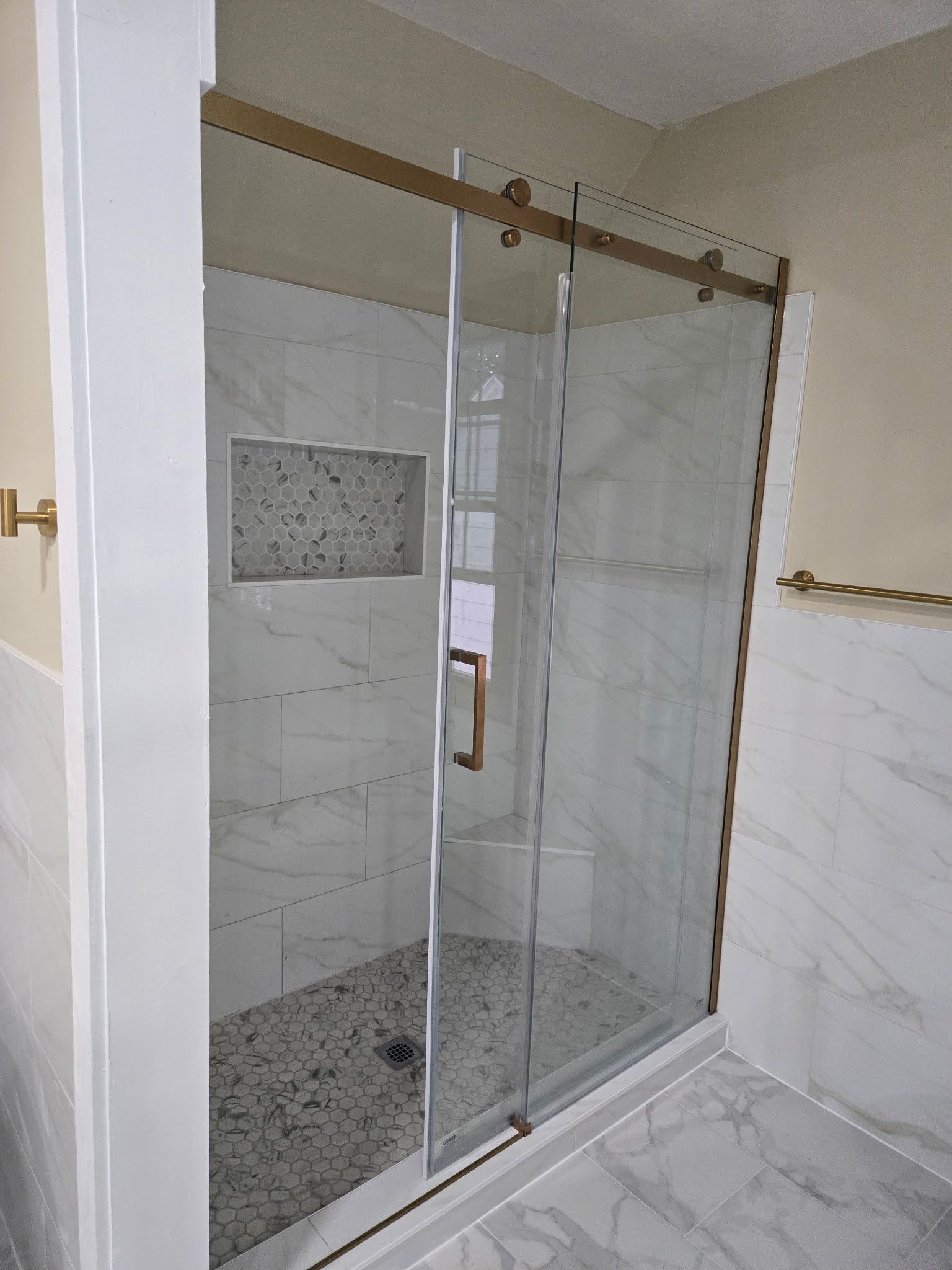 Shower with sliding glass doors, marble tile, and a gold-colored hardware.