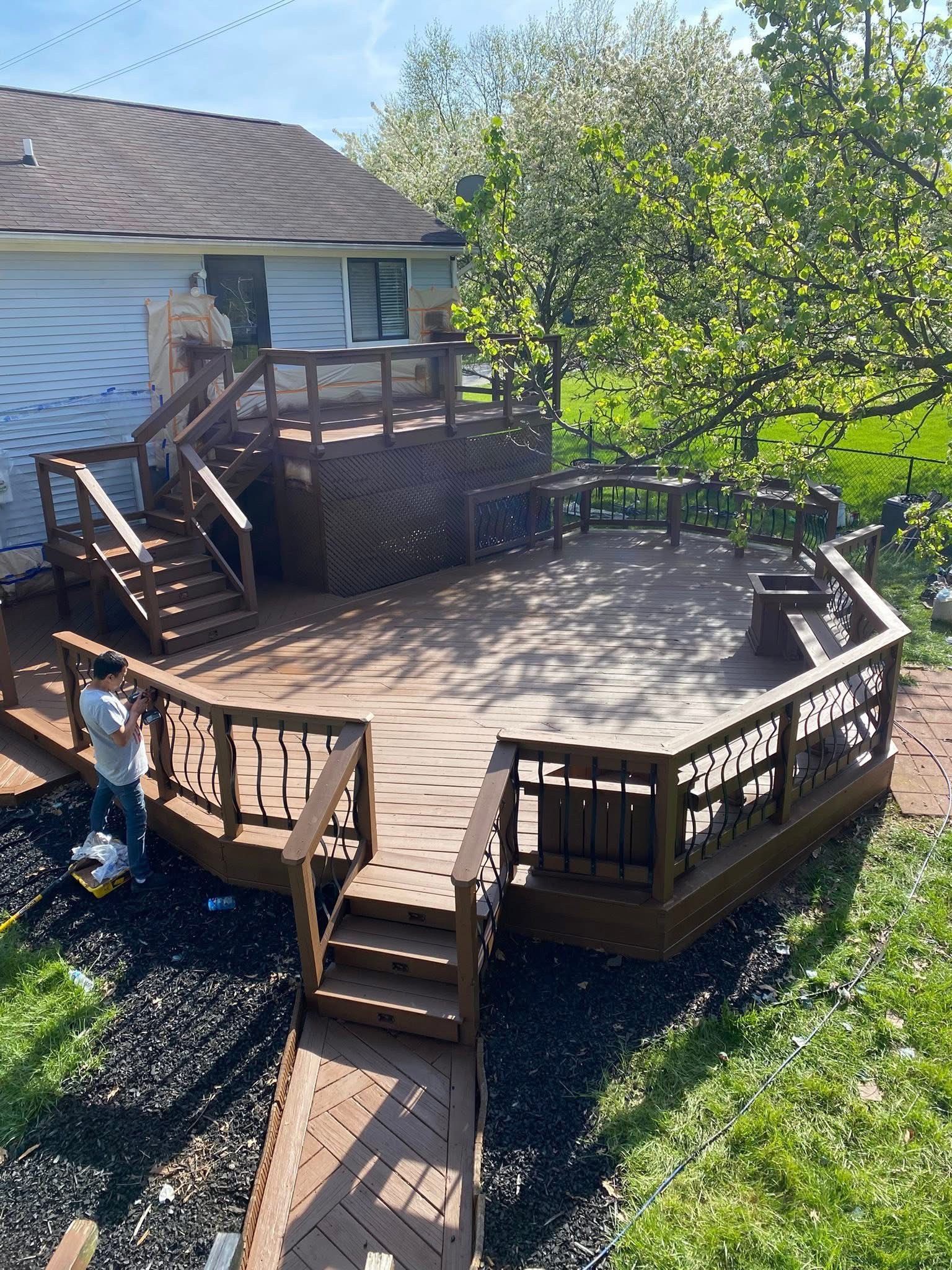 Brown wooden deck with steps, a person painting, and surrounding green trees.