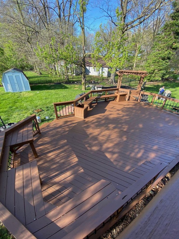 Wooden deck with built-in seating in a yard, shed and trees visible in the background.
