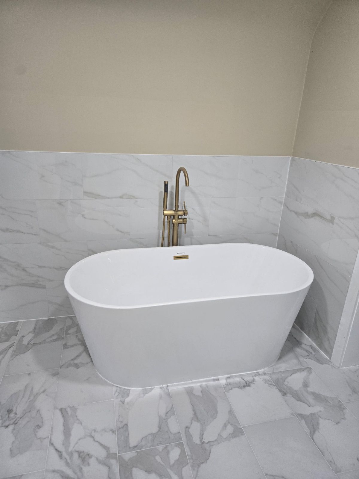 Oval white bathtub with gold faucet in a marble-tiled bathroom.
