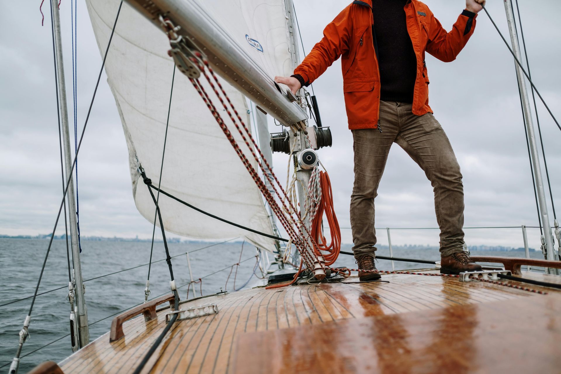 A man in an orange jacket is standing on the deck of a sailboat.