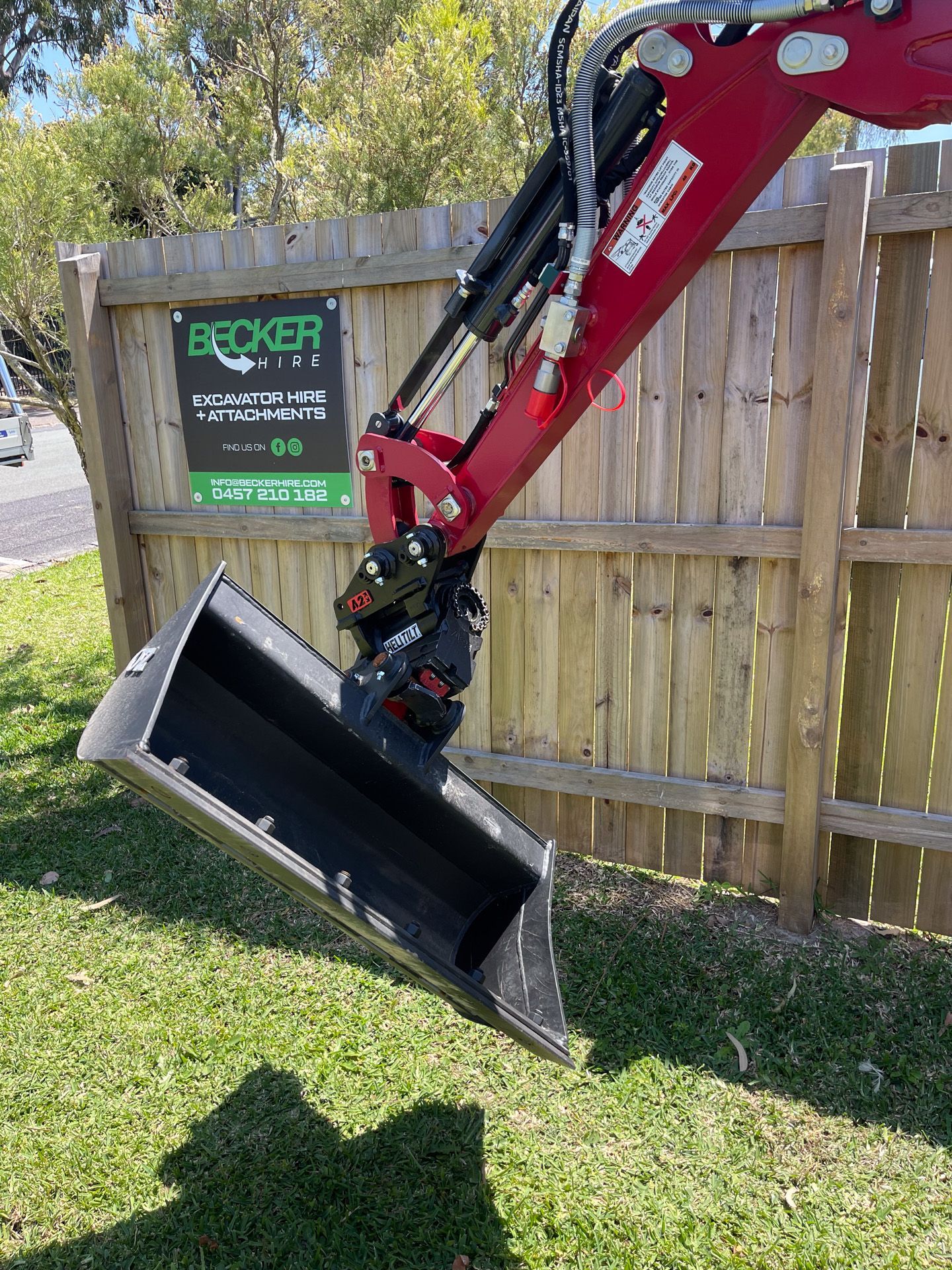 A person operating a small excavator, digging a trench in a wooded area with brown soil.