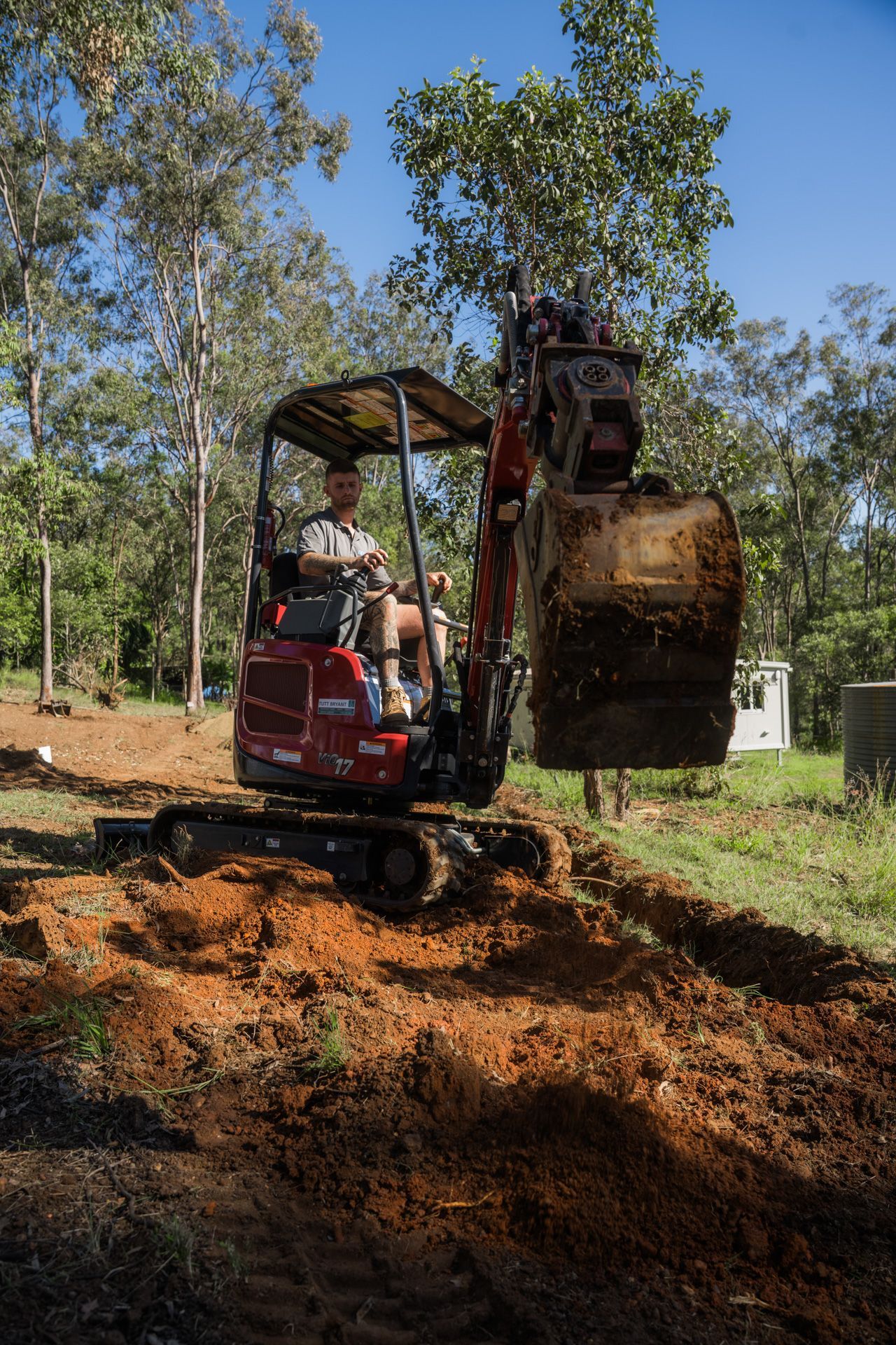 Red excavator on a construction site; license plate reads T392C3.