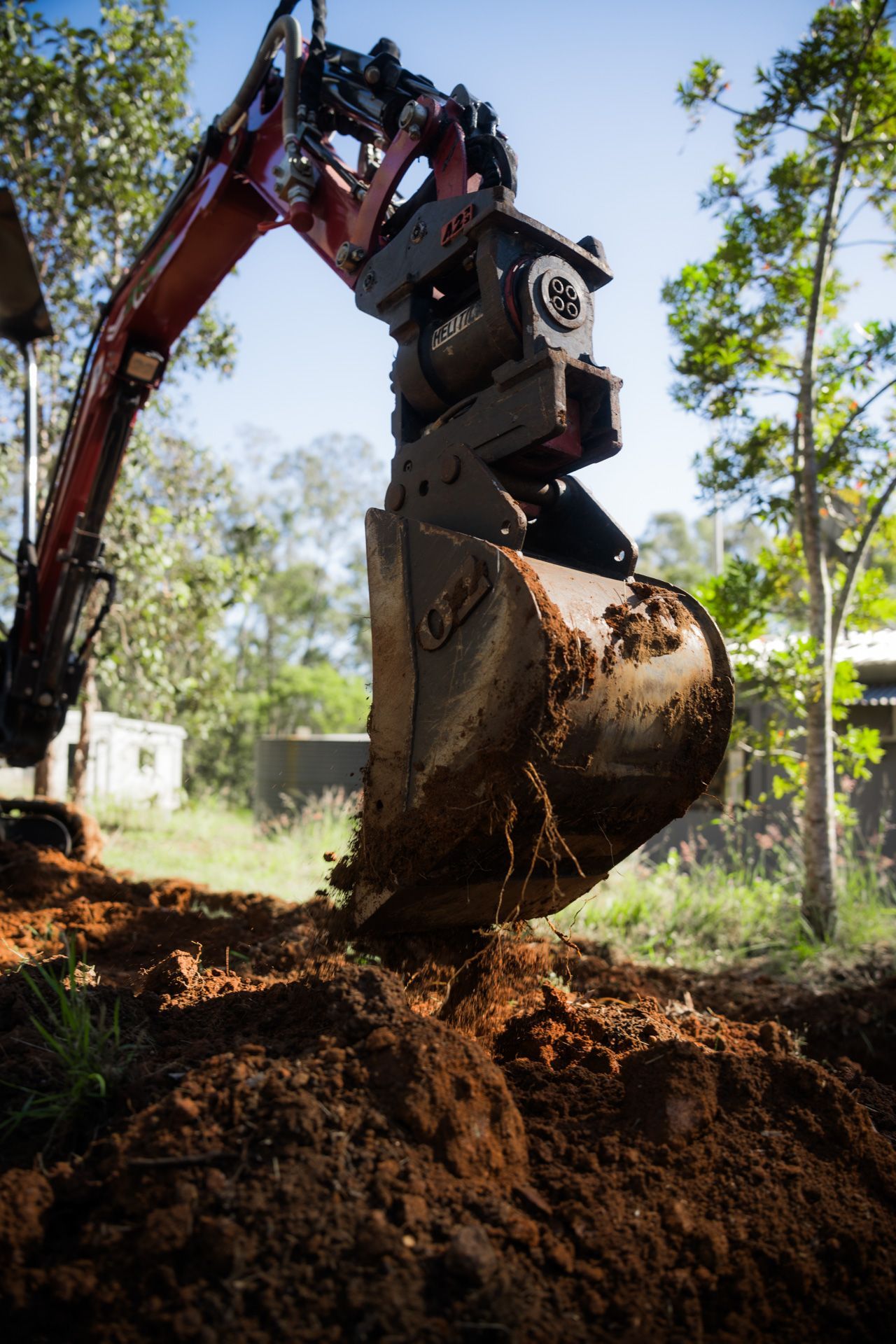 A small excavator bucket scoops up dirt in an outdoor setting.