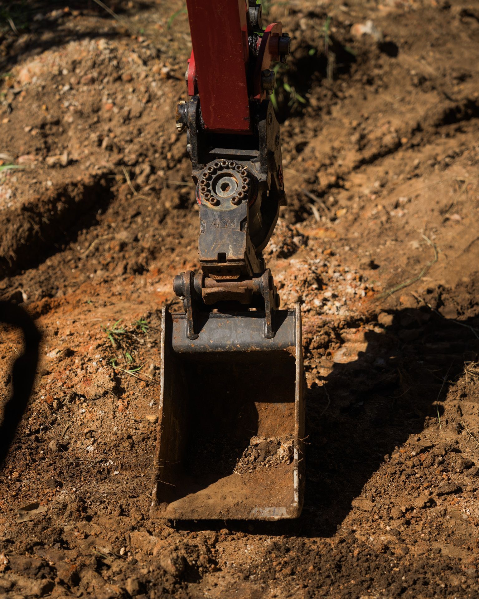 A small excavator bucket scoops up dirt in an outdoor setting.