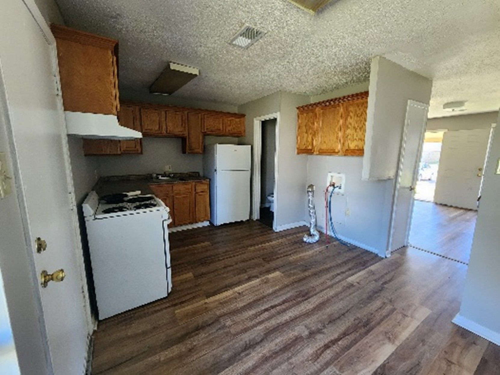 Kitchen with wood cabinets, white appliances, and wood-look flooring. Includes open doorway.