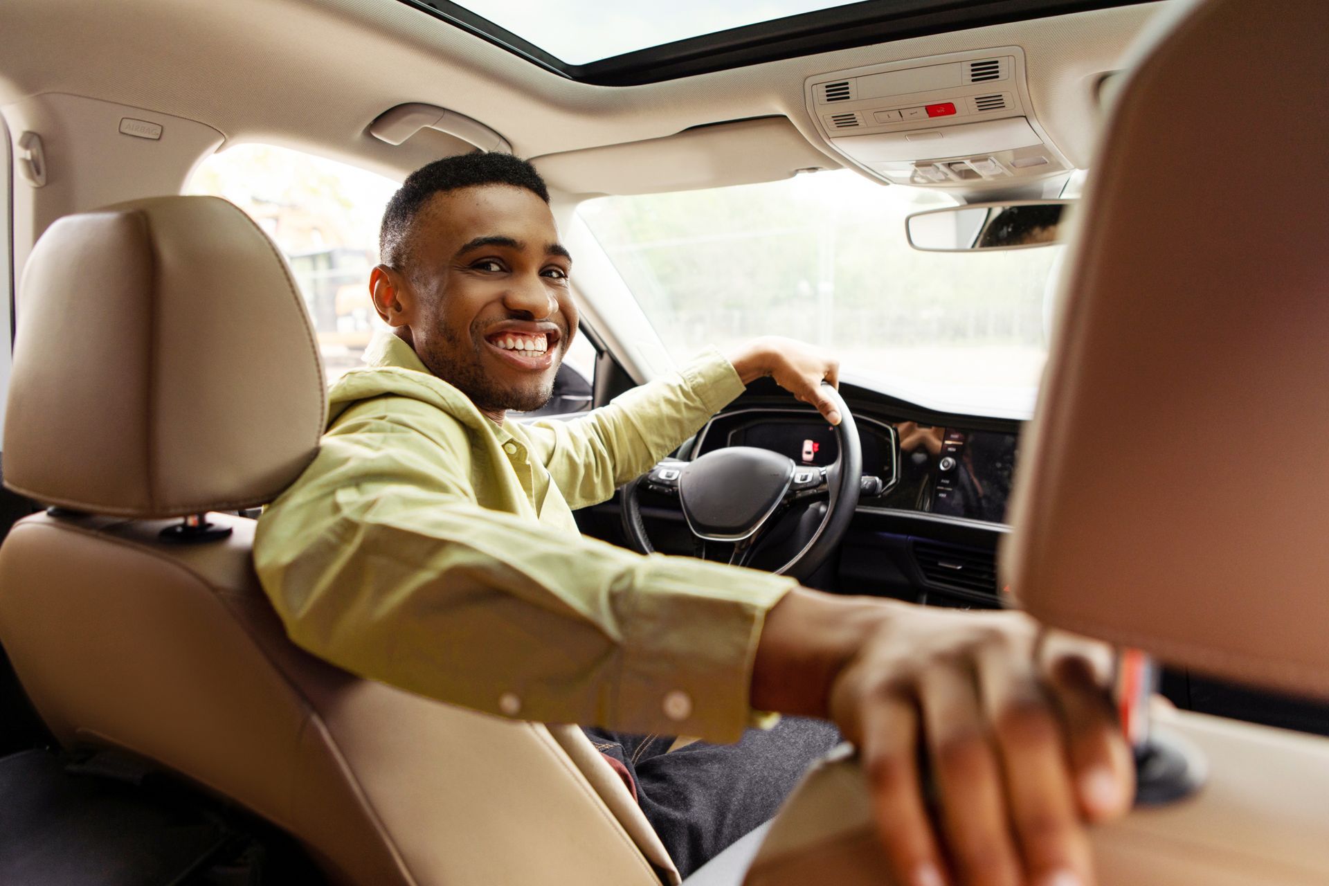 A man is driving a car with a woman sitting in the back seat talking on a cell phone.