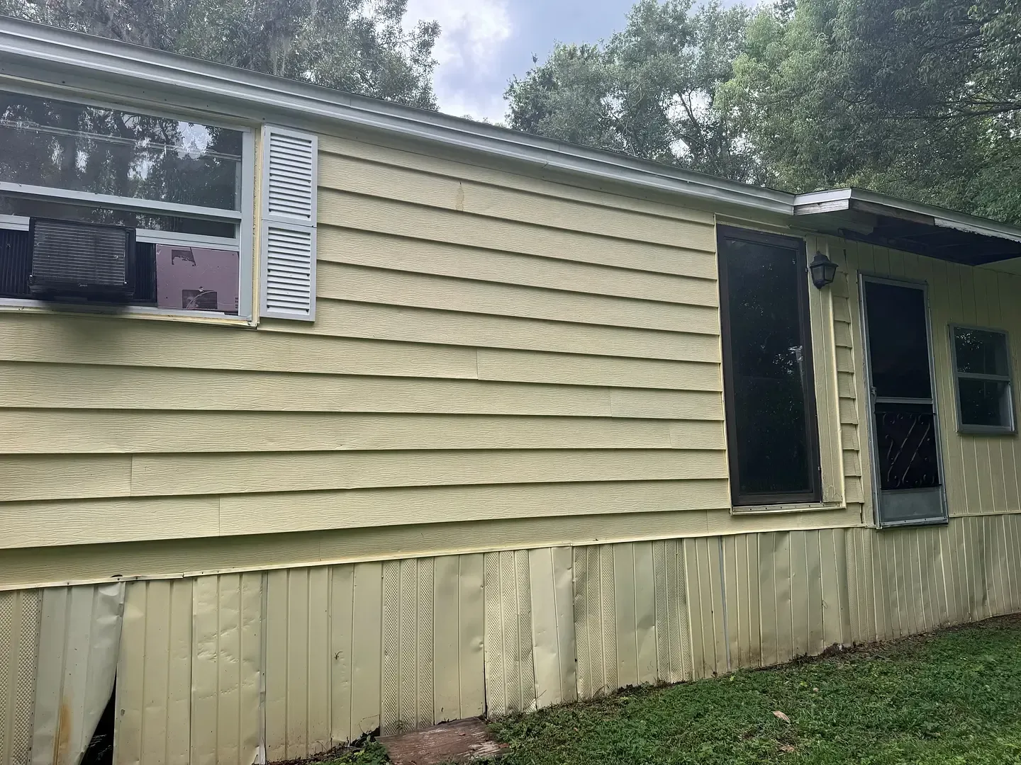 Yellow-sided, single-story building with a dark door, small windows, and visible air conditioning unit.
