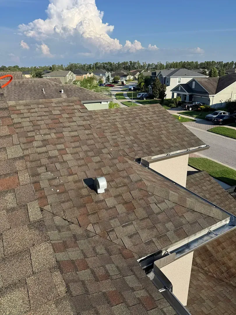 Overhead view of a shingle roof with some dark and light shingles in a residential neighborhood.