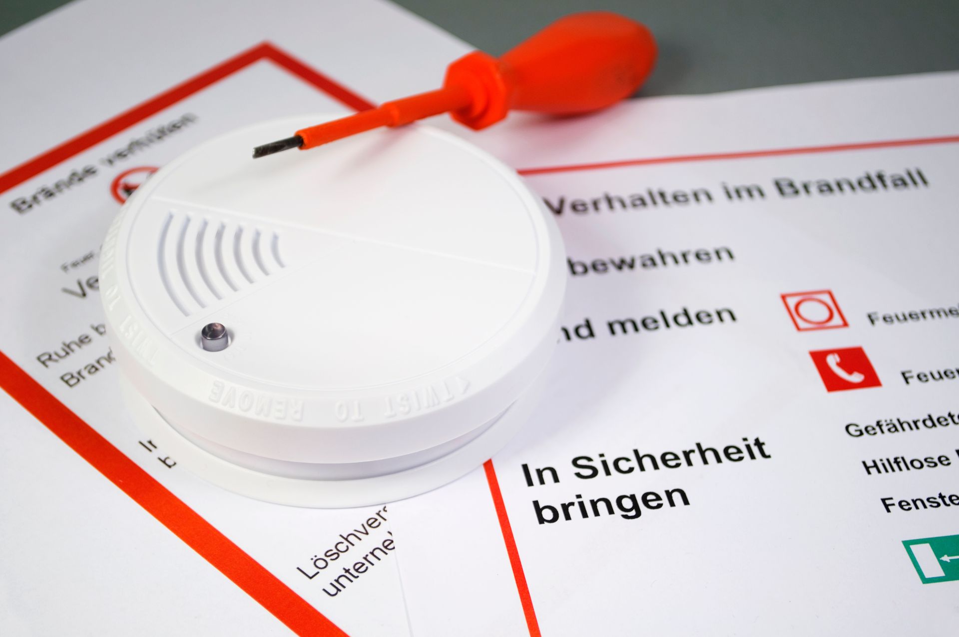 Ein Rauchmelder liegt auf einem Papier mit der Aufschrift „in Sicherheit bringen“